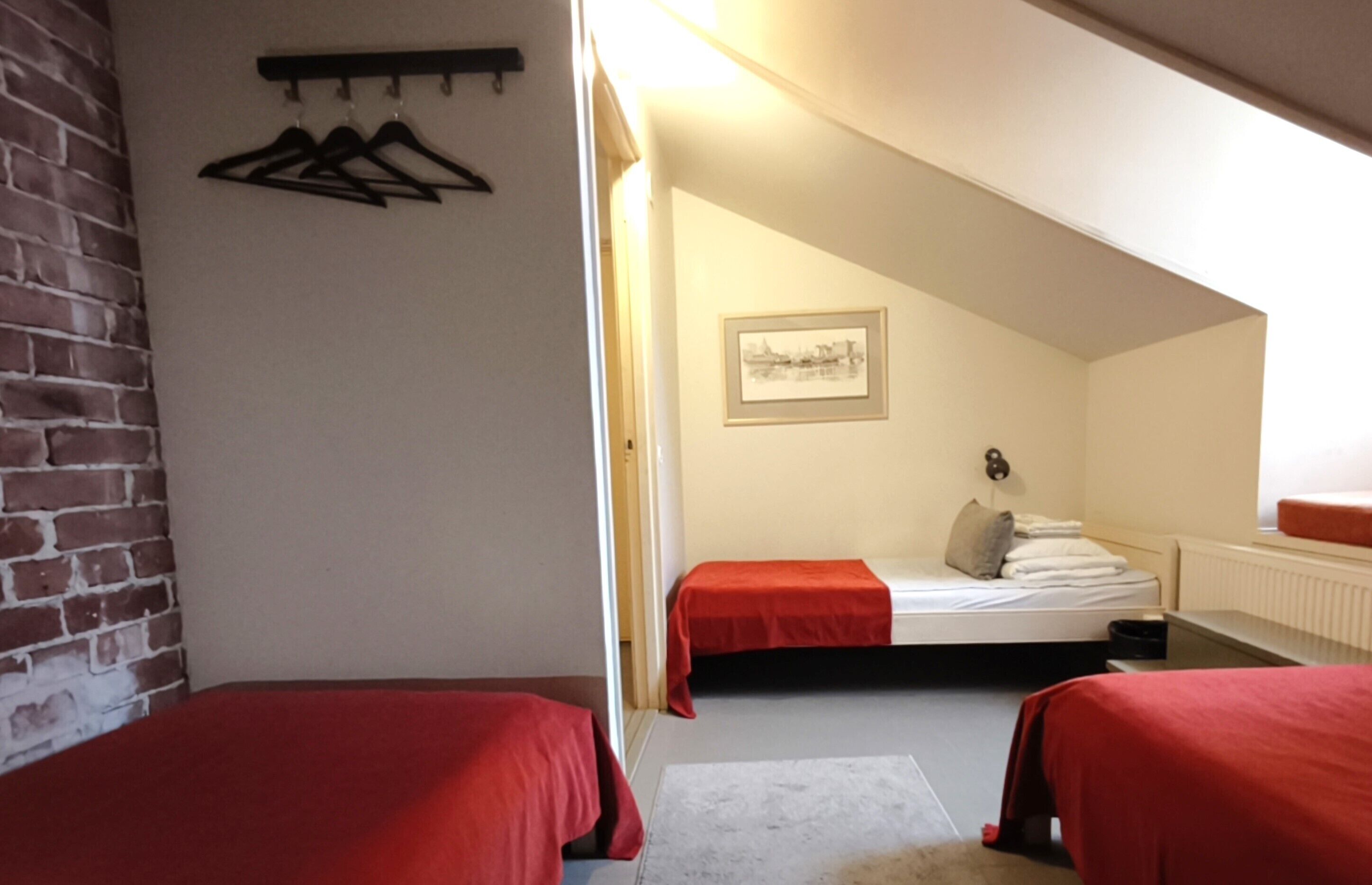 A room with two beds, a brick wall, a coat rack, and a framed picture on the wall.