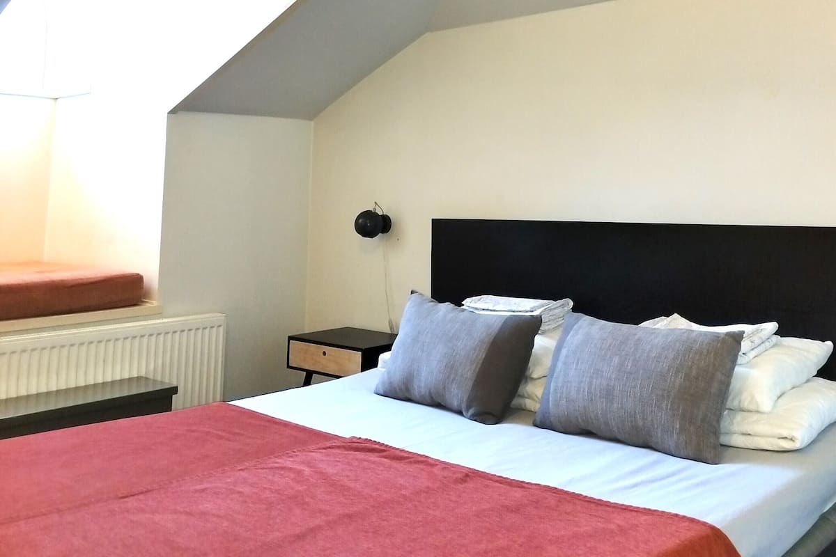 A bedroom with a bed, a nightstand, a lamp, and a window.