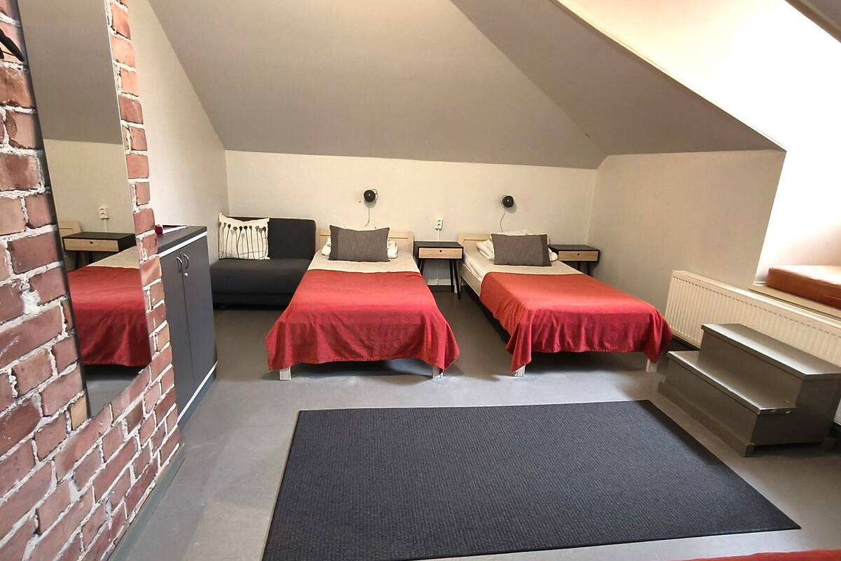 A dormitory room with two beds, a desk, a chair, a radiator, and a brick wall.