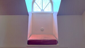 A room with a sloped ceiling, a window with a white frame, and a small circular light fixture on the wall. - Hostel Suomenlinna (Helsinki)