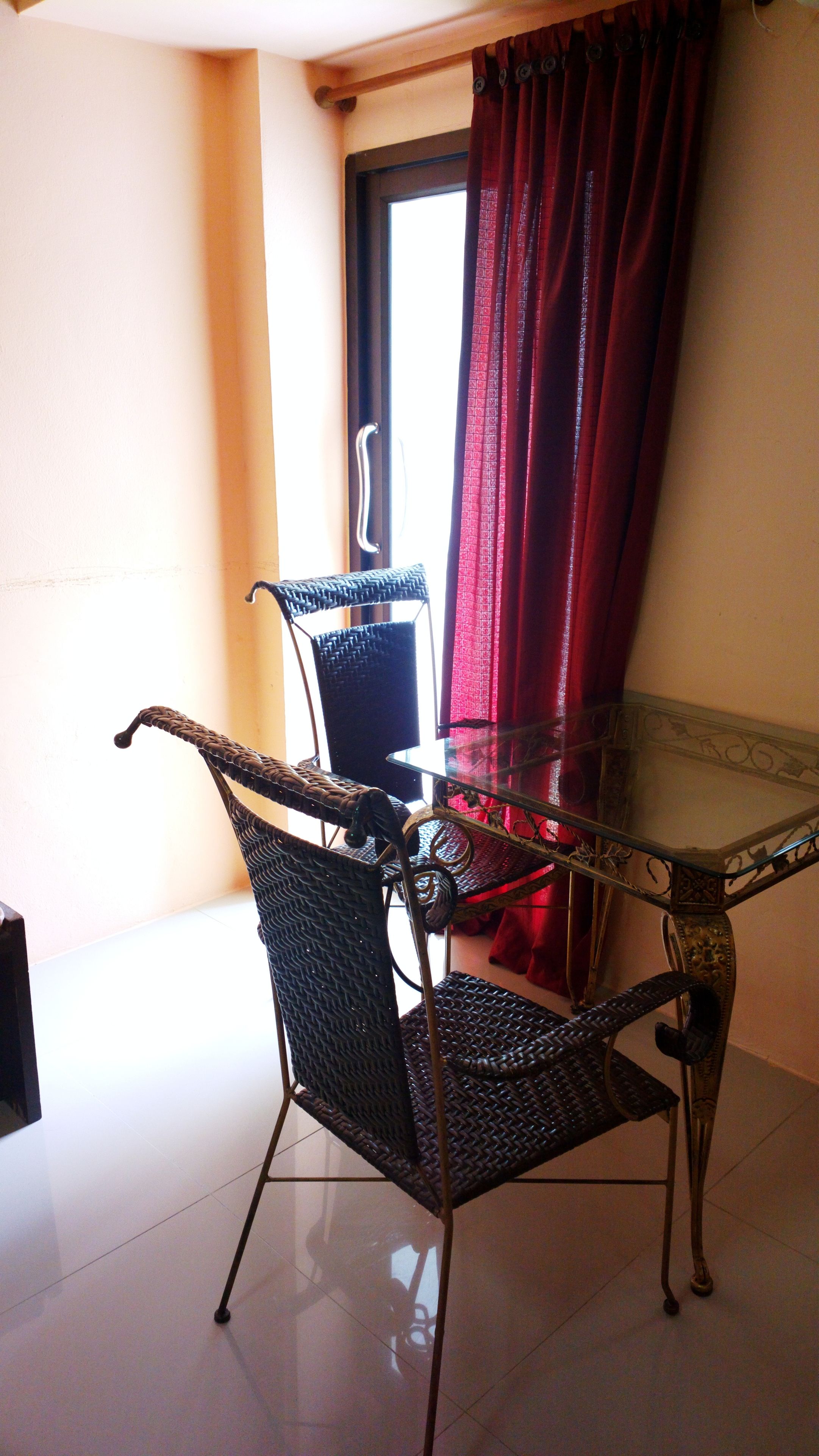 A dining area with a glass table and wicker chairs, a red curtain, and a door with a handle.