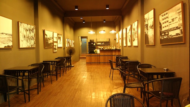 A restaurant with wooden flooring, black chairs, and tables. There are framed pictures on the walls and a bar area in the center. - Huahin Euro City Hotel (Hua Hin)
