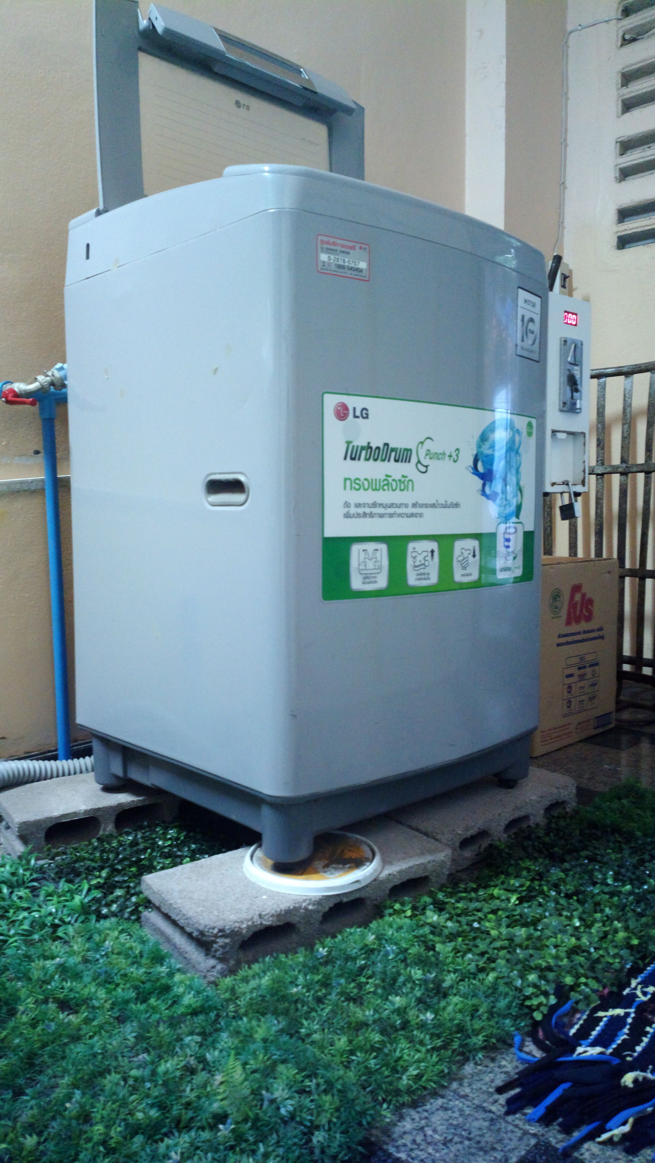 A white LG TurboDrum water heater with a green label, placed outdoors on concrete blocks with grass around.