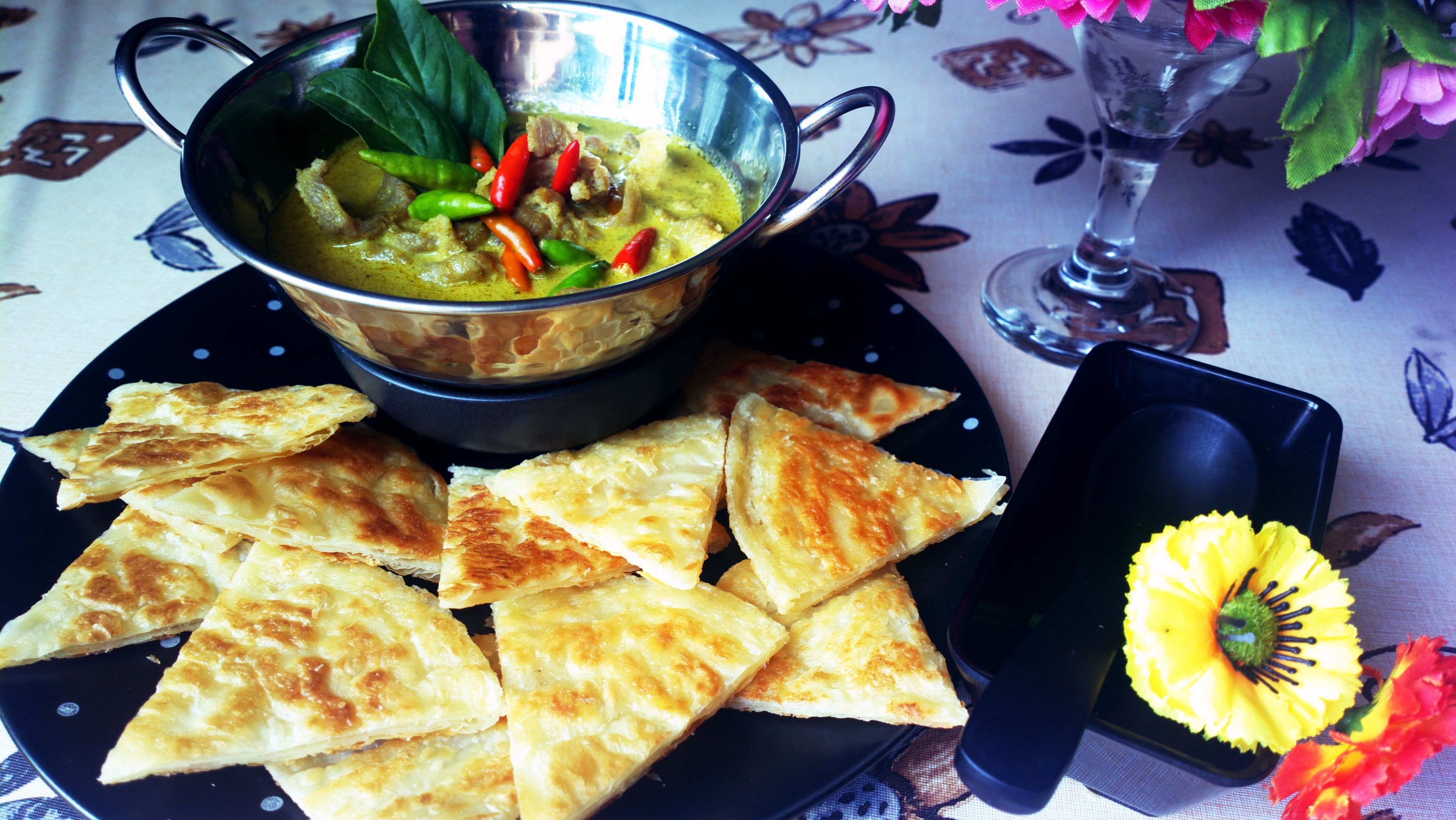 Una comida que incluye un tazón de sopa, pequeños pasteles triangulares y un jarrón pequeño con una flor amarilla.
