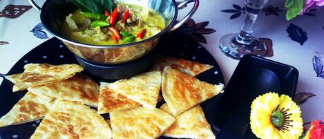 Una comida que incluye un tazón de sopa, pequeños pasteles triangulares y un jarrón pequeño con una flor amarilla.