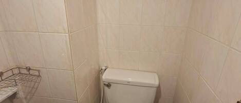 Une petite salle de bain avec des toilettes, une poubelle et une étagère en métal.