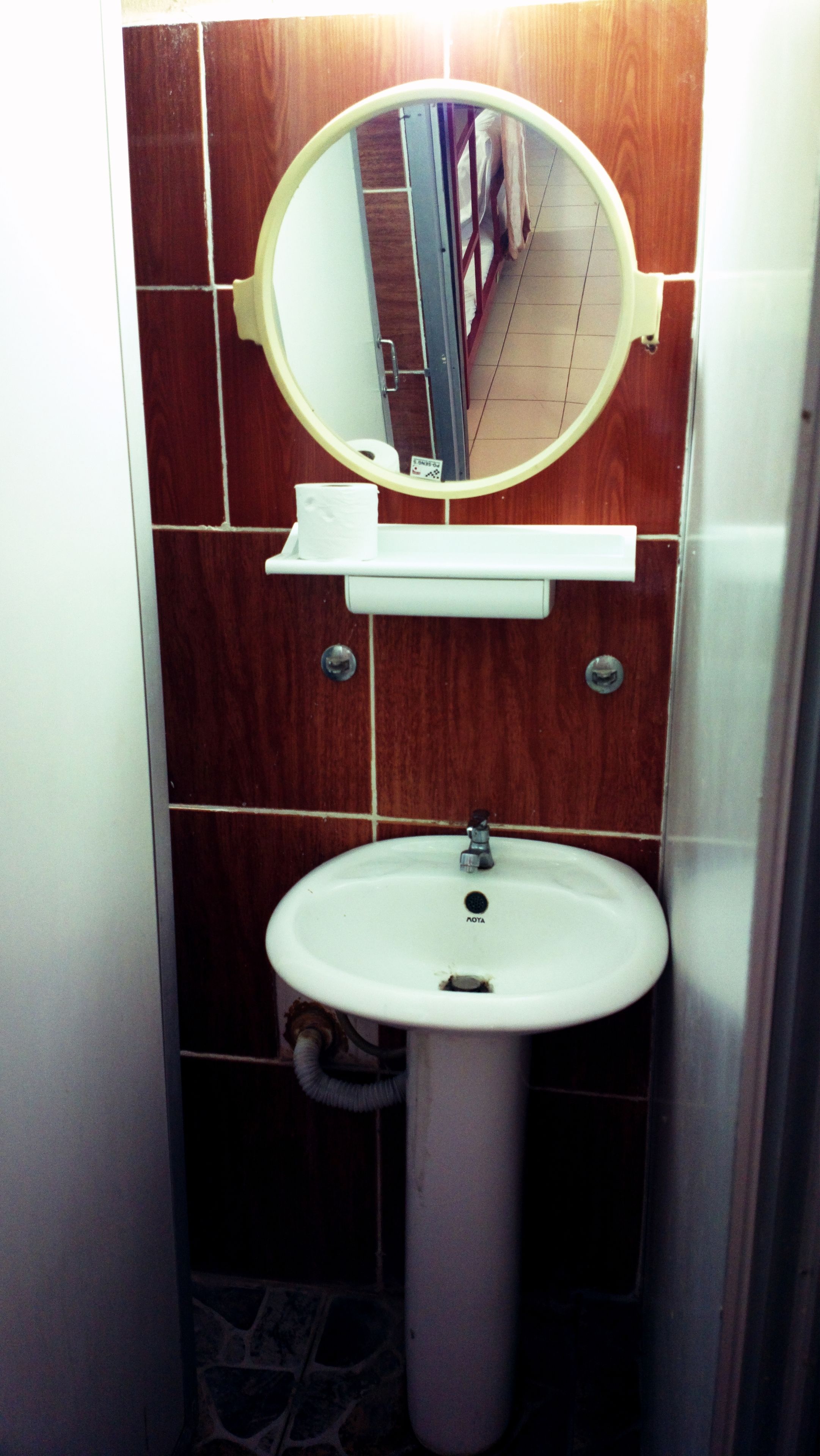 Un baño con un lavamanos pedestal blanco, un espejo encima y un dispensador de papel higiénico en la pared.