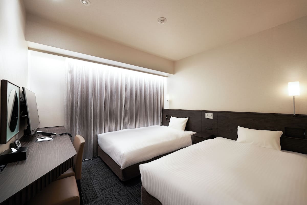 Une chambre d’hôtel avec deux lits, un bureau avec un ordinateur et une télévision.