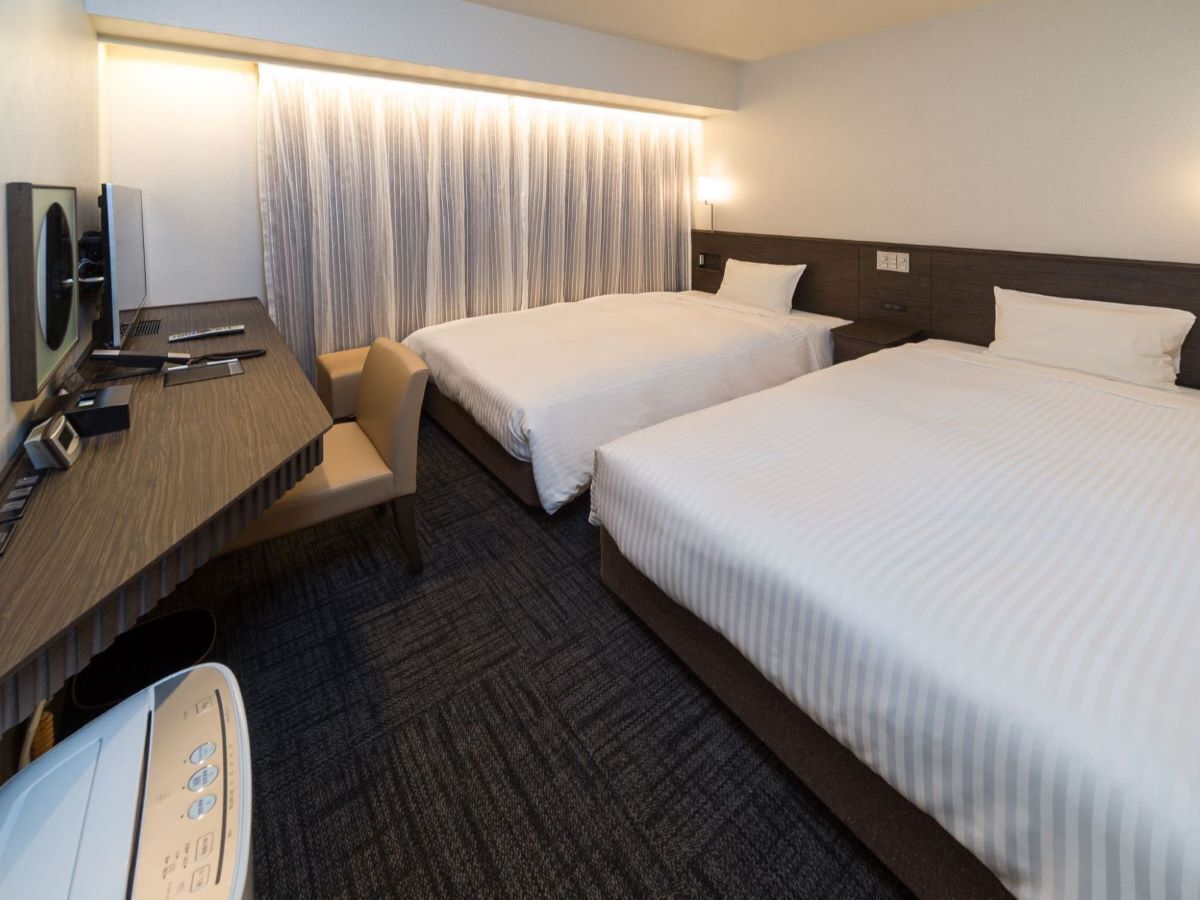 Quarto de hotel com duas camas, uma mesa de escritório com um computador e uma cadeira.
