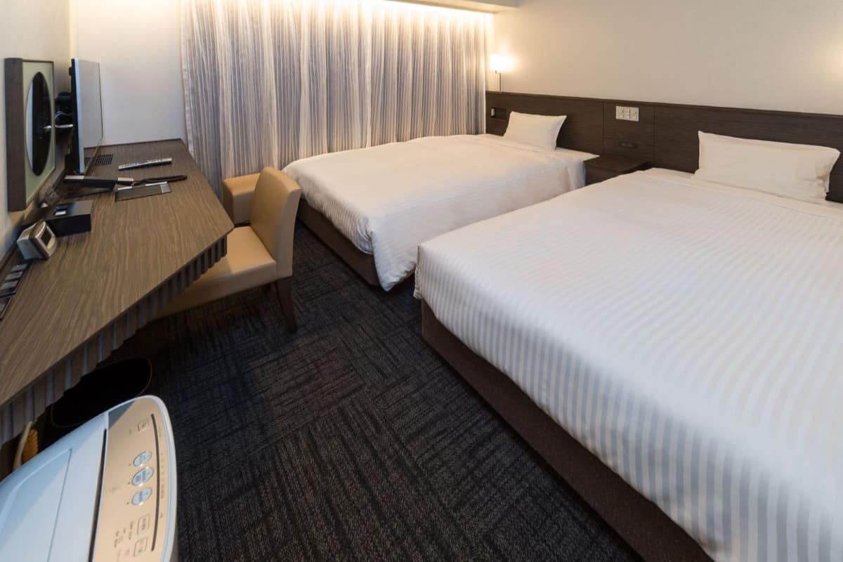 Une chambre d’hôtel avec deux lits, un bureau équipé d’un ordinateur et une chaise.