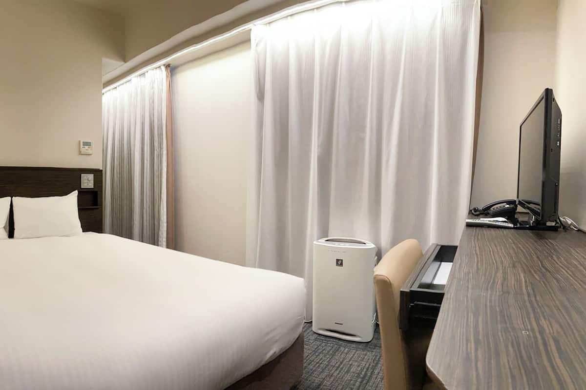 Une chambre d’hôtel avec un grand lit, un bureau équipé d’un ordinateur, une lampe et une fenêtre avec des rideaux.