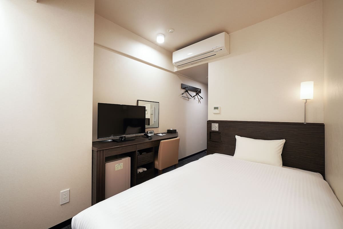 Une chambre d’hôtel équipée d’un lit, d’un bureau avec un ordinateur, d’une télévision et d’un appareil de climatisation.