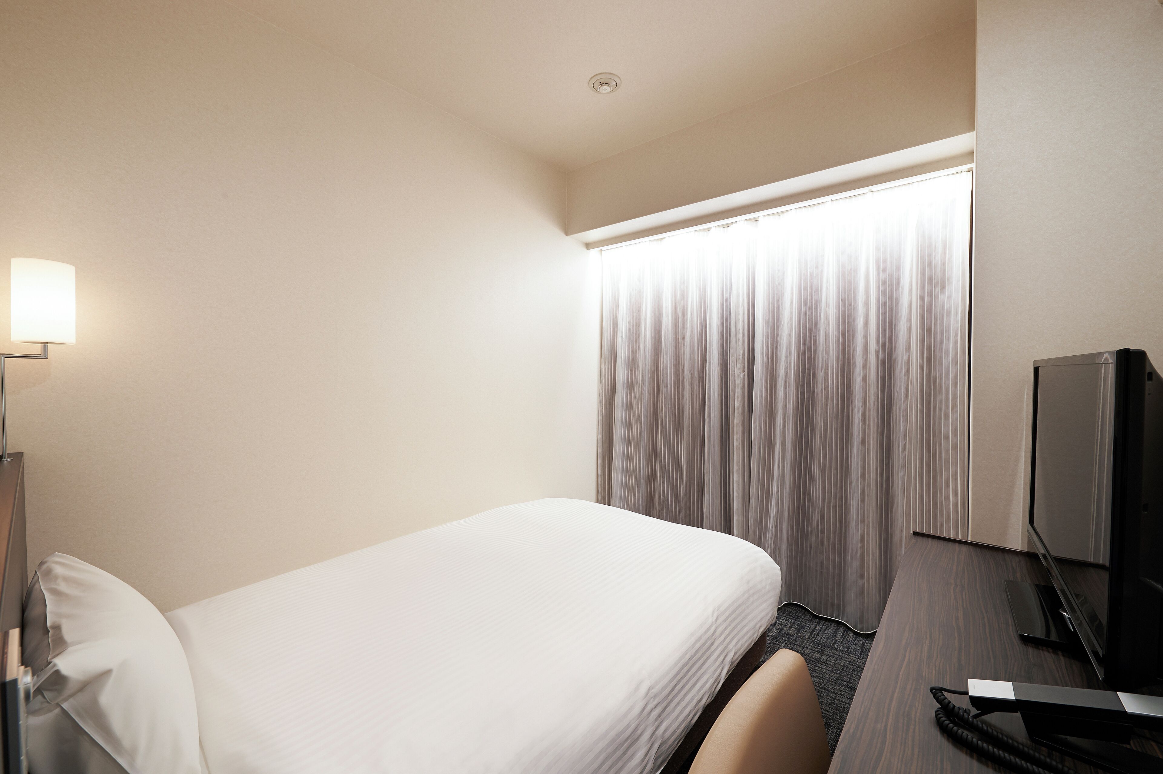 A hotel room with a bed, a desk with a computer, a lamp, and a window with curtains.