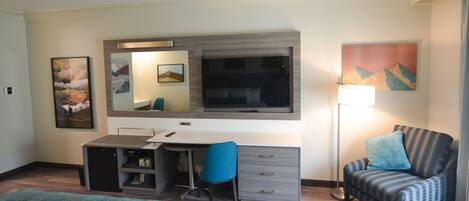 A hotel room with a bed, a desk, a chair, a TV, and artwork on the walls.
