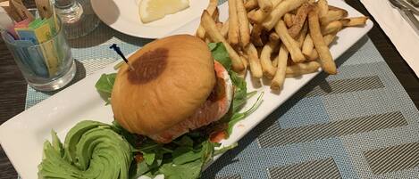 A meal consisting of a burger with lettuce and avocado, a side of fries, and a glass of iced tea on a table.