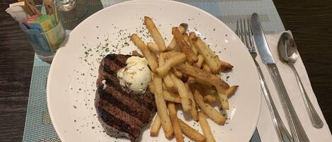 A plate with steak, fries, and a scoop of ice cream, accompanied by a glass of a red beverage and a lemon wedge on a table.