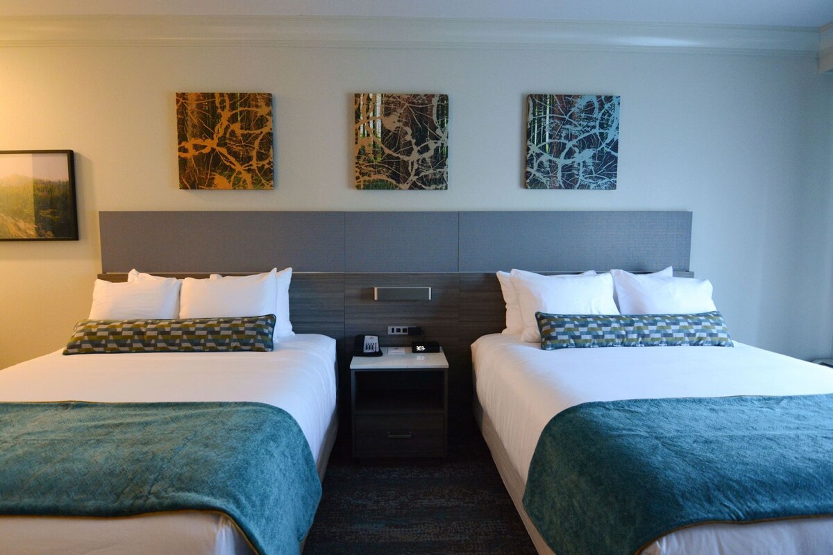 A hotel room with two beds, a nightstand, and three abstract wall art pieces.