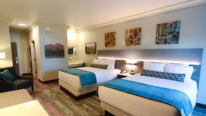 A hotel room with two beds, a desk, and a chair. There are three paintings on the wall.