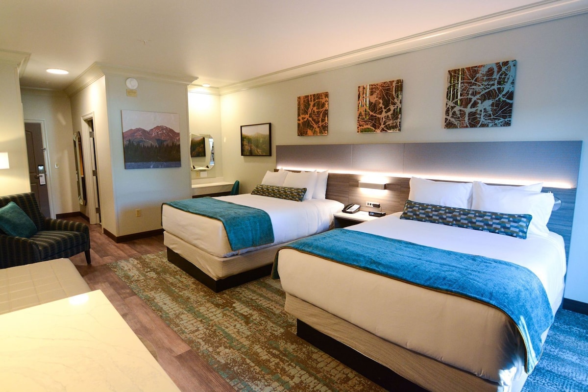 Una habitación de hotel con dos camas, un escritorio, una silla y obras de arte en las paredes.