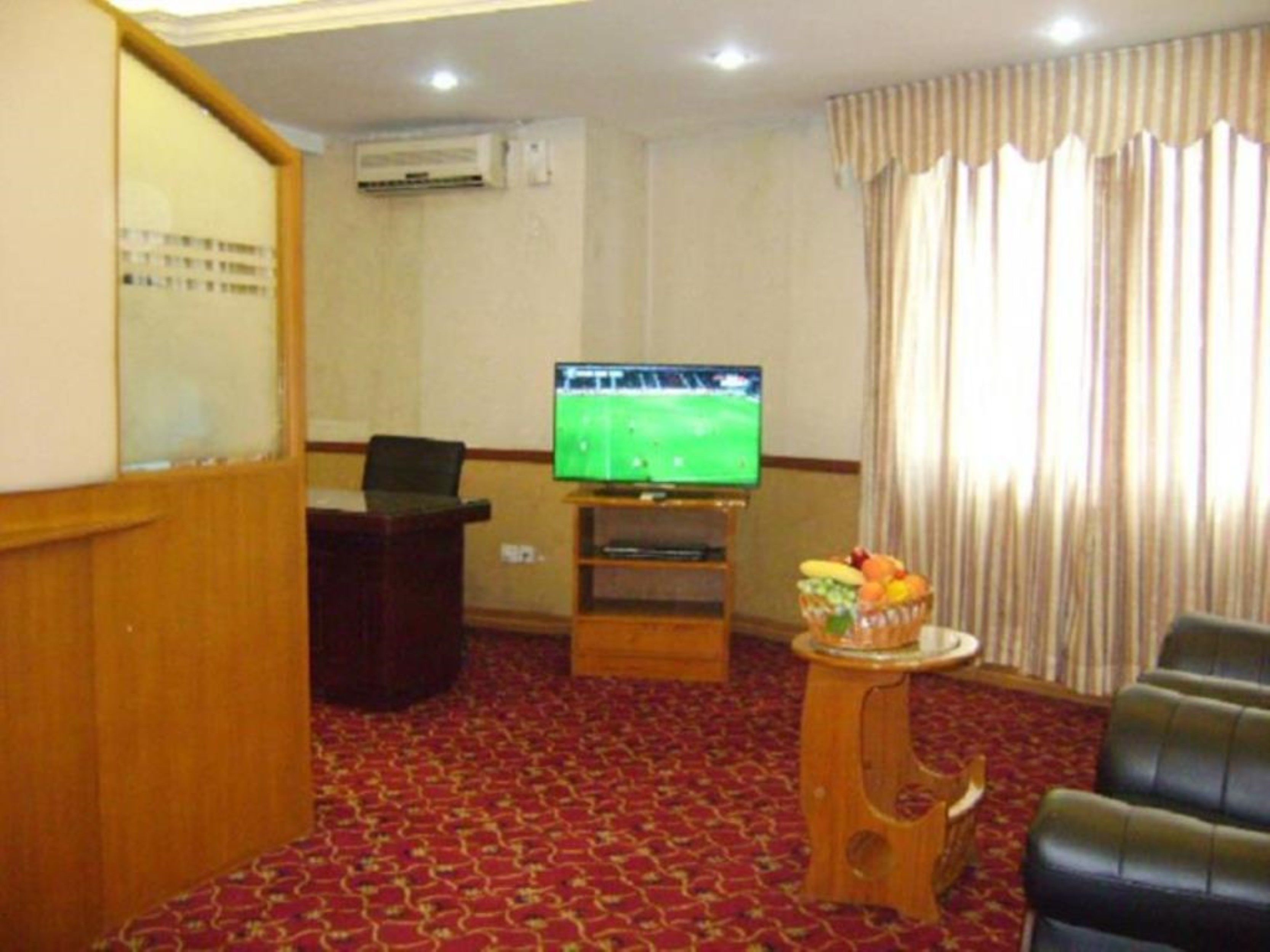 A living room with a television, a desk, a chair, and a small table with fruit.