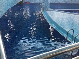 A swimming pool with clear blue water, a tiled edge, and metal handrails.