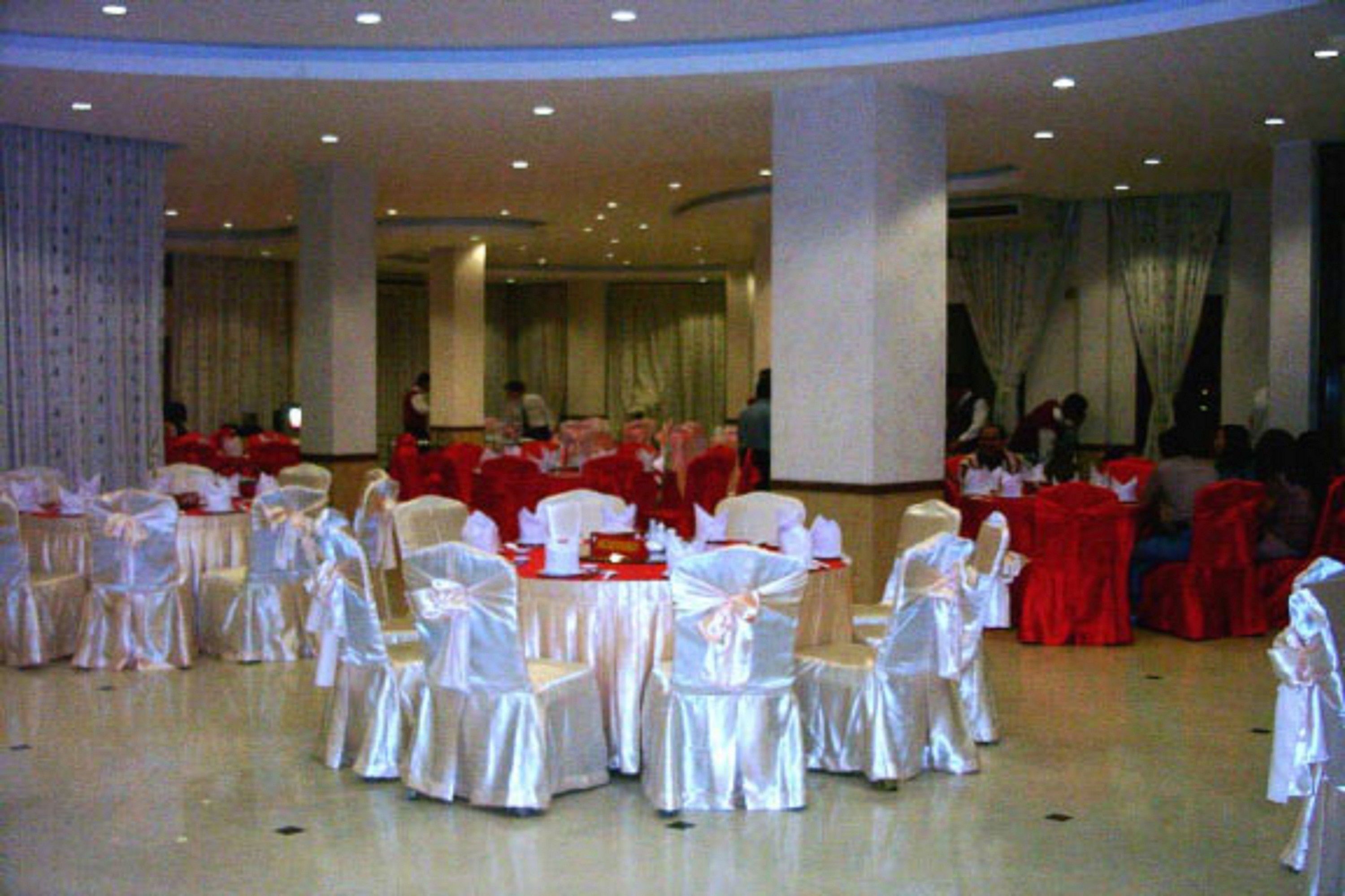A banquet hall with round tables and chairs, some covered in red and others in white.