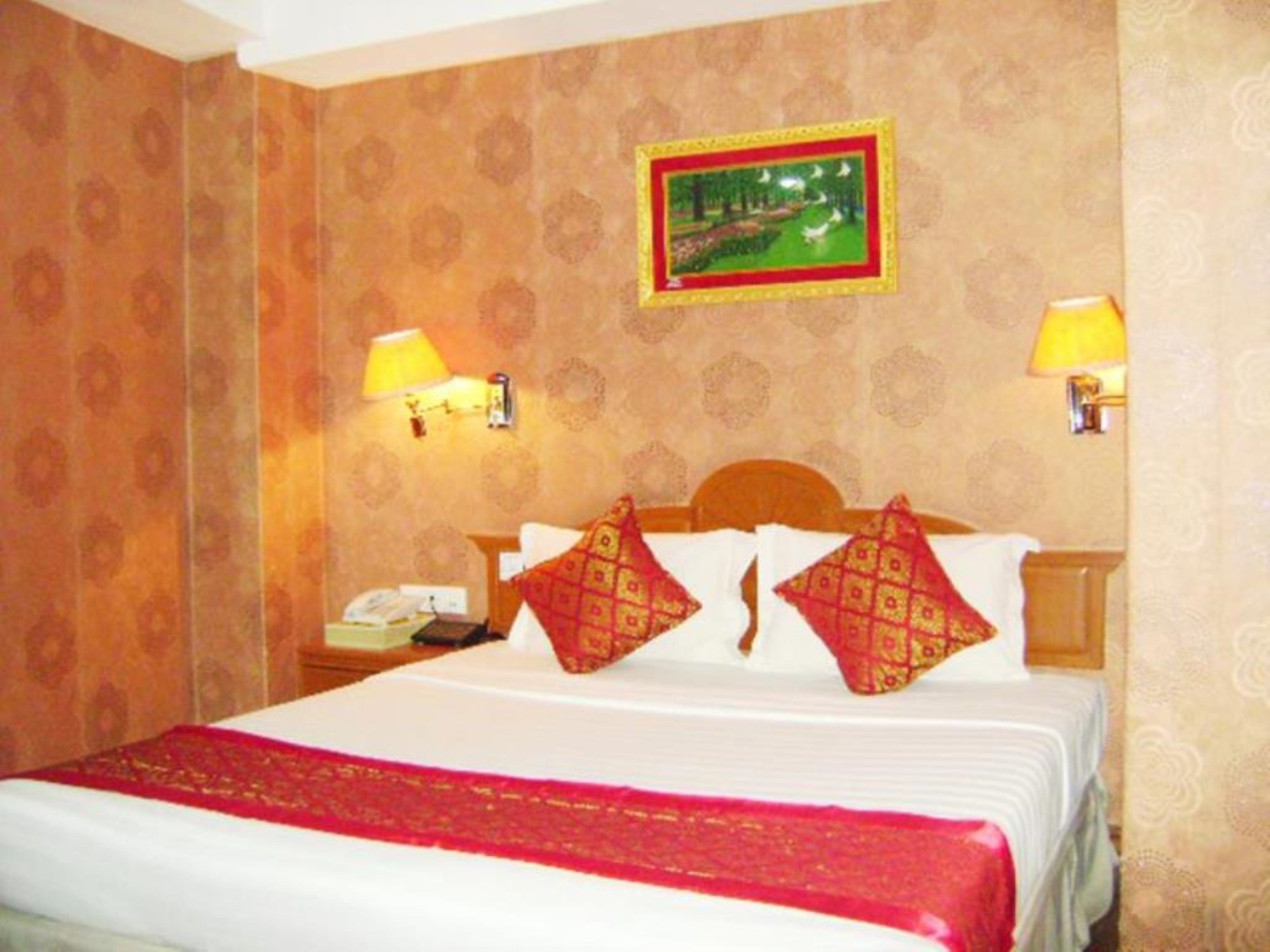 A hotel room with a neatly made bed, two bedside lamps, a telephone, and a framed picture on the wall.