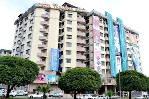 A multi-story hotel with balconies, a prominent sign reading "EXCEL TREASURE HOTEL," and several large advertisements on the facade.