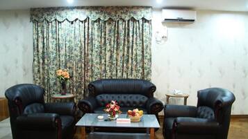 Una habitación con un sofá de cuero negro, dos sillones, una mesita con un florero y una cortina estampada.
