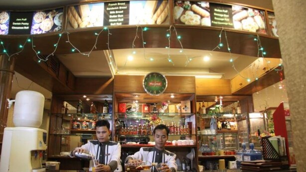 A bar area with a menu board, bar stools, and a counter. - Excel Treasure Hotel (Yangon)