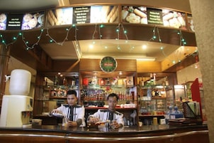 A bar area with a menu board, bar stools, and a counter.