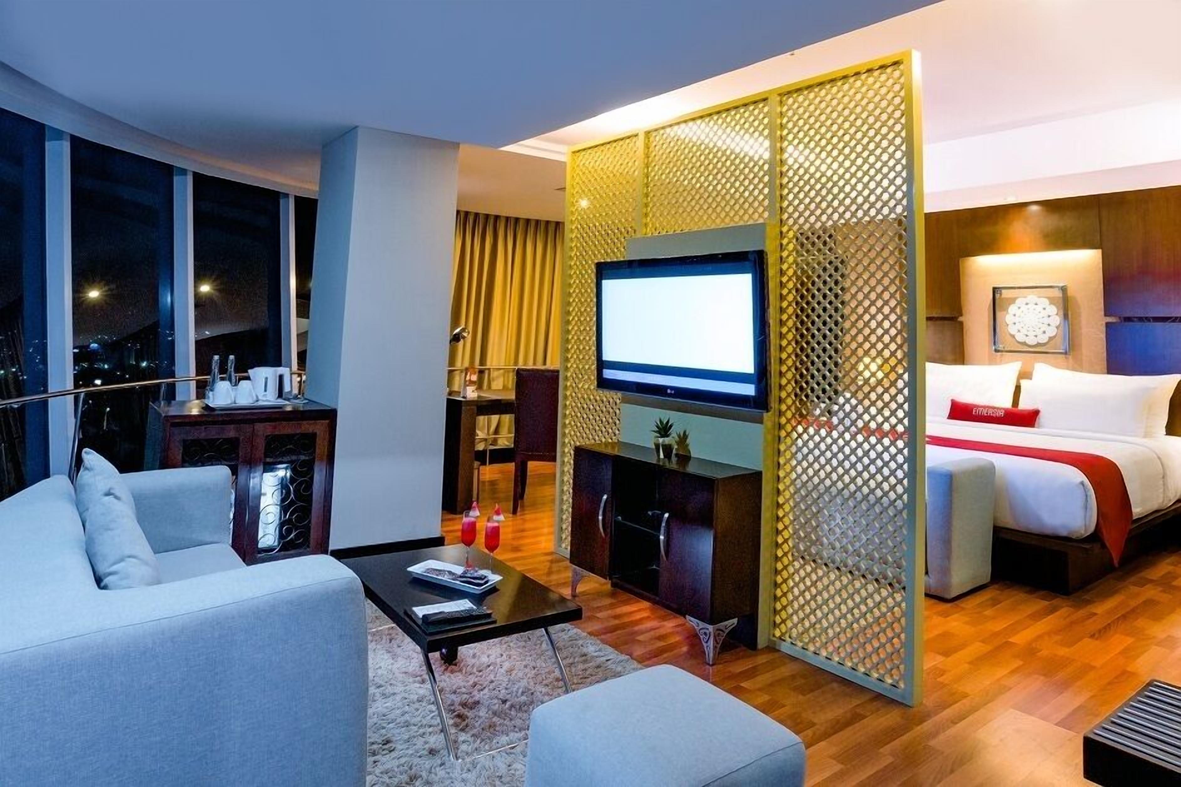 Ett modernt hotellrum med en stor TV, en soffa, en säng och en matplats.