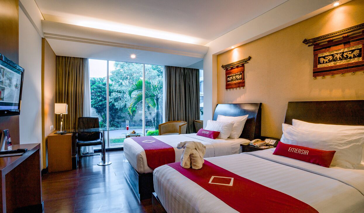 A hotel room with two beds, a desk, a chair, and a TV.