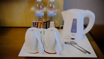 Una mesa con dos tazas blancas, una tetera eléctrica blanca y una cuchara sobre un servilleta blanca.