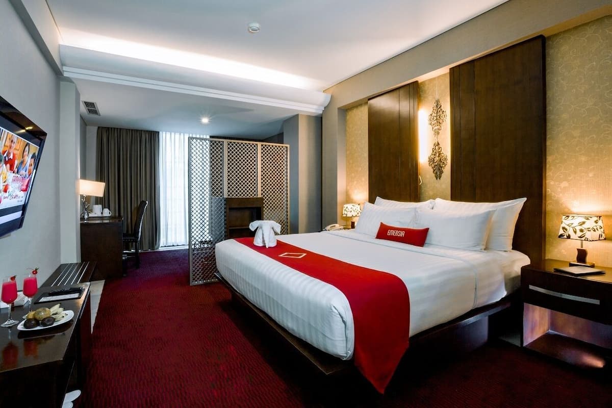 Une chambre d’hôtel avec un grand lit, un bureau avec un téléphone, une petite table avec des boissons et un téléviseur fixé au mur.