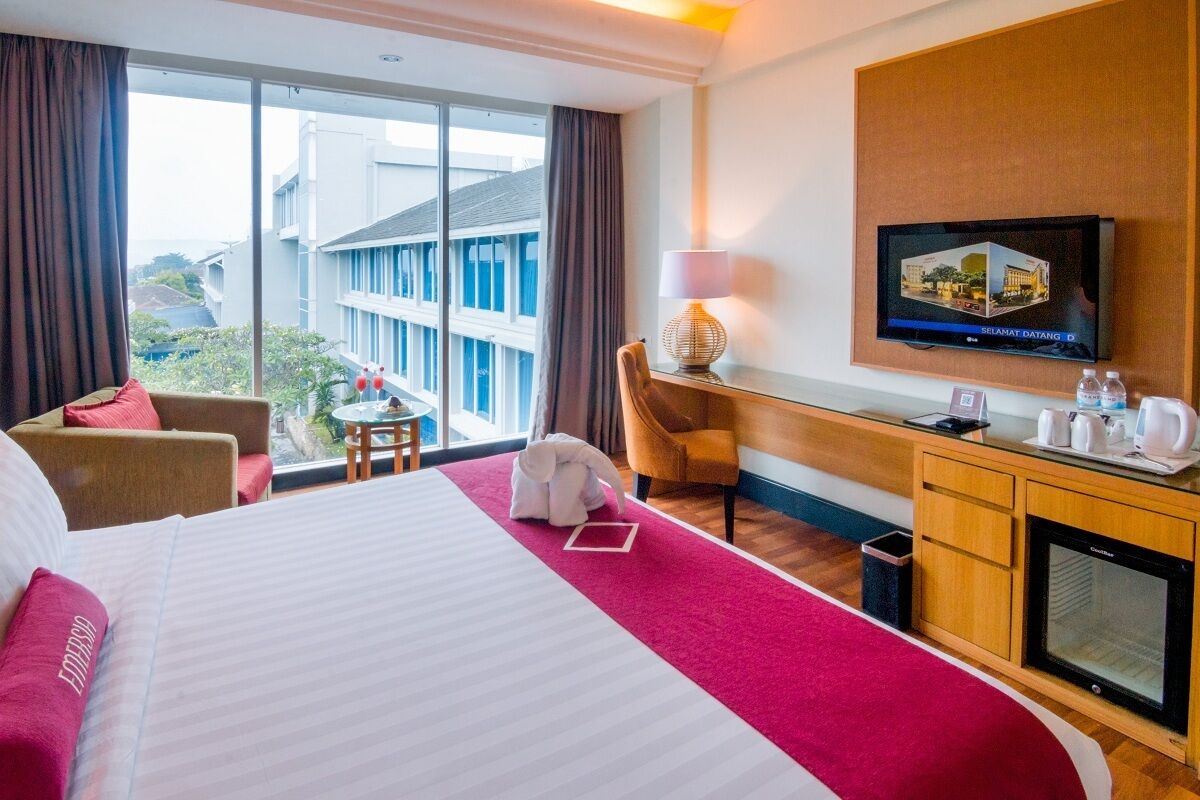 A hotel room with a large bed, a desk with a computer, a TV, and a view of buildings outside.