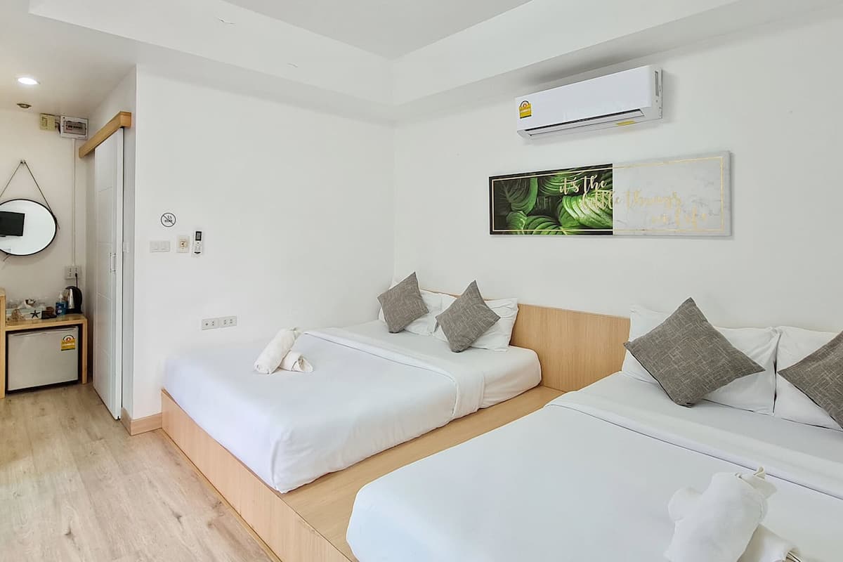 A hotel room with two beds, a small desk, a mirror, an air conditioner, and a wall-mounted artwork.