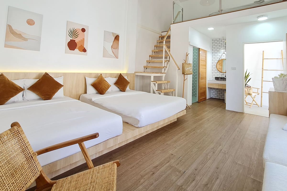 A hotel room with two beds, a wooden floor, a staircase, and a kitchen area.
