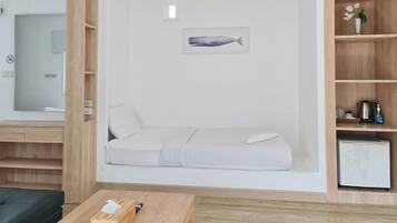Et minimalistisk rum med en hvid sofa, en lille seng, en træhylde med et maleri af en fisk og et hvidt køleskab.