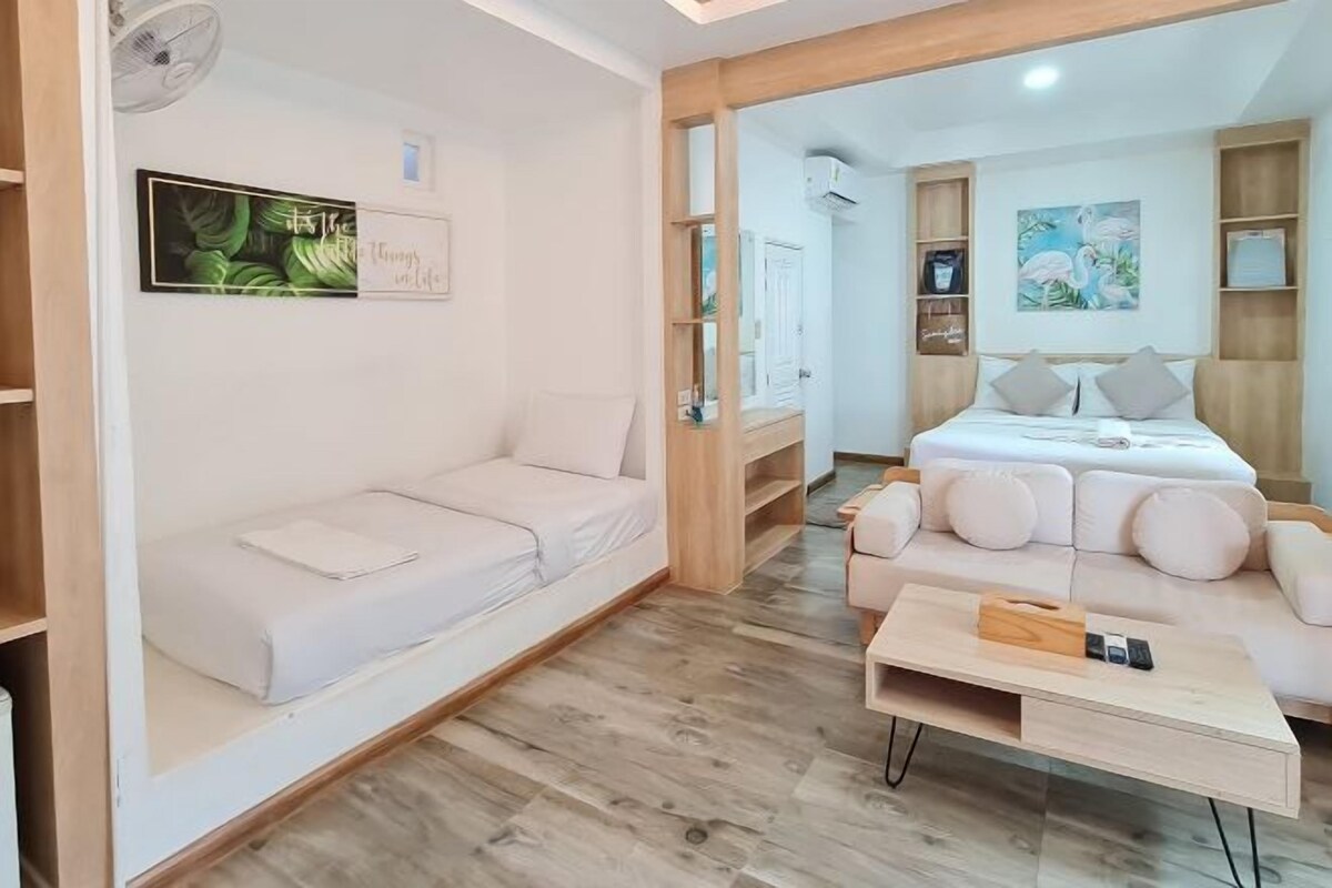 Quarto de hotel moderno com um sofá branco, uma mesa de centro de madeira e uma cama com roupa de cama branca.