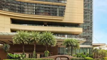 Un edificio moderno con fachada curva, una entrada ajardinada con palmeras y un letrero que dice "RAFFLES JAKARTA".