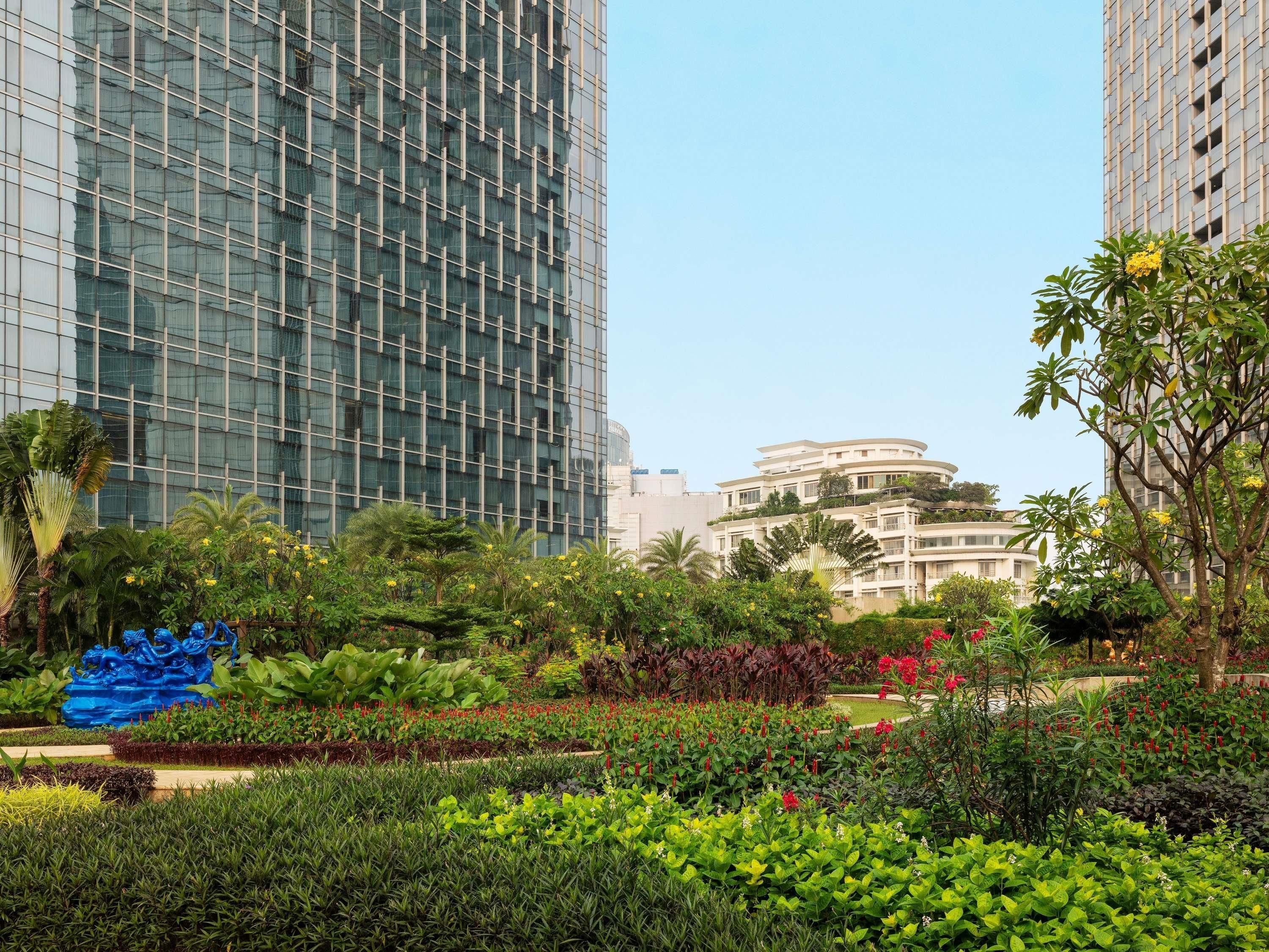 A landscaped garden with various plants and a blue sculpture, surrounded by modern buildings.