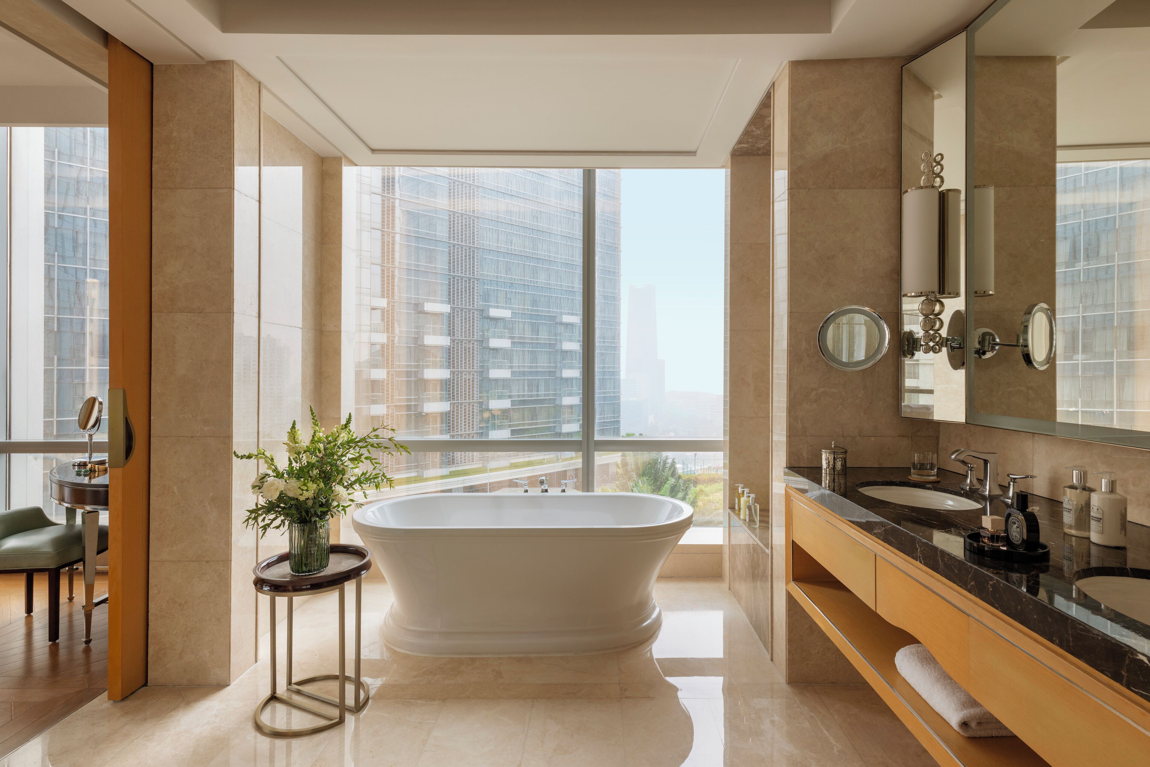 Un baño moderno con una bañera independiente, ventanas amplias y vistas a edificios altos.
