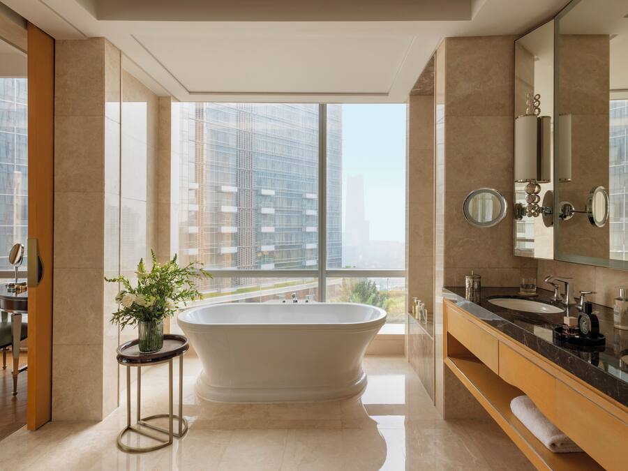 Un baño moderno con una bañera independiente, ventanas amplias y vistas a edificios altos.