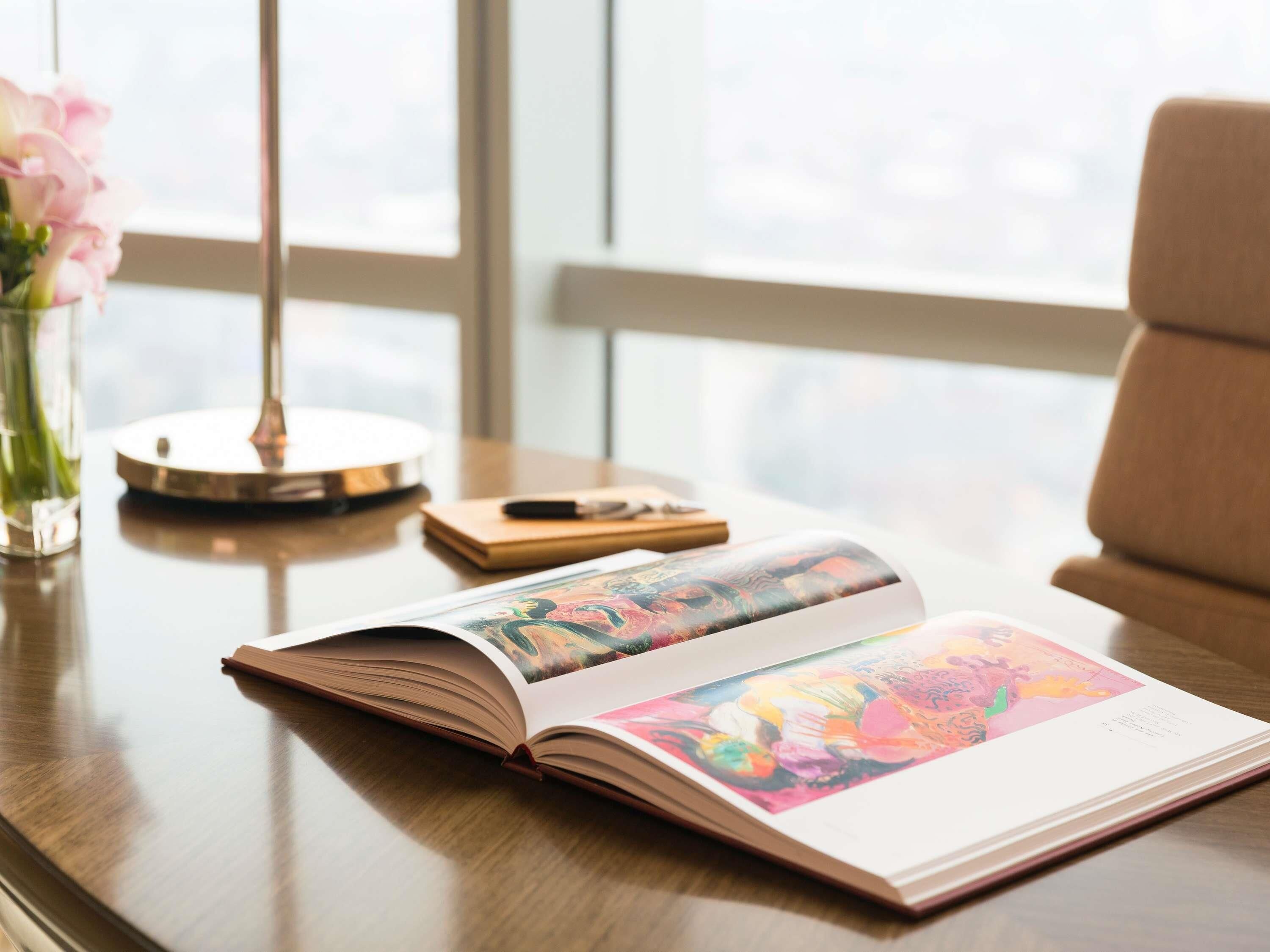 Un libro abierto sobre una mesa de madera, con una lámpara, un cuaderno y un bolígrafo.