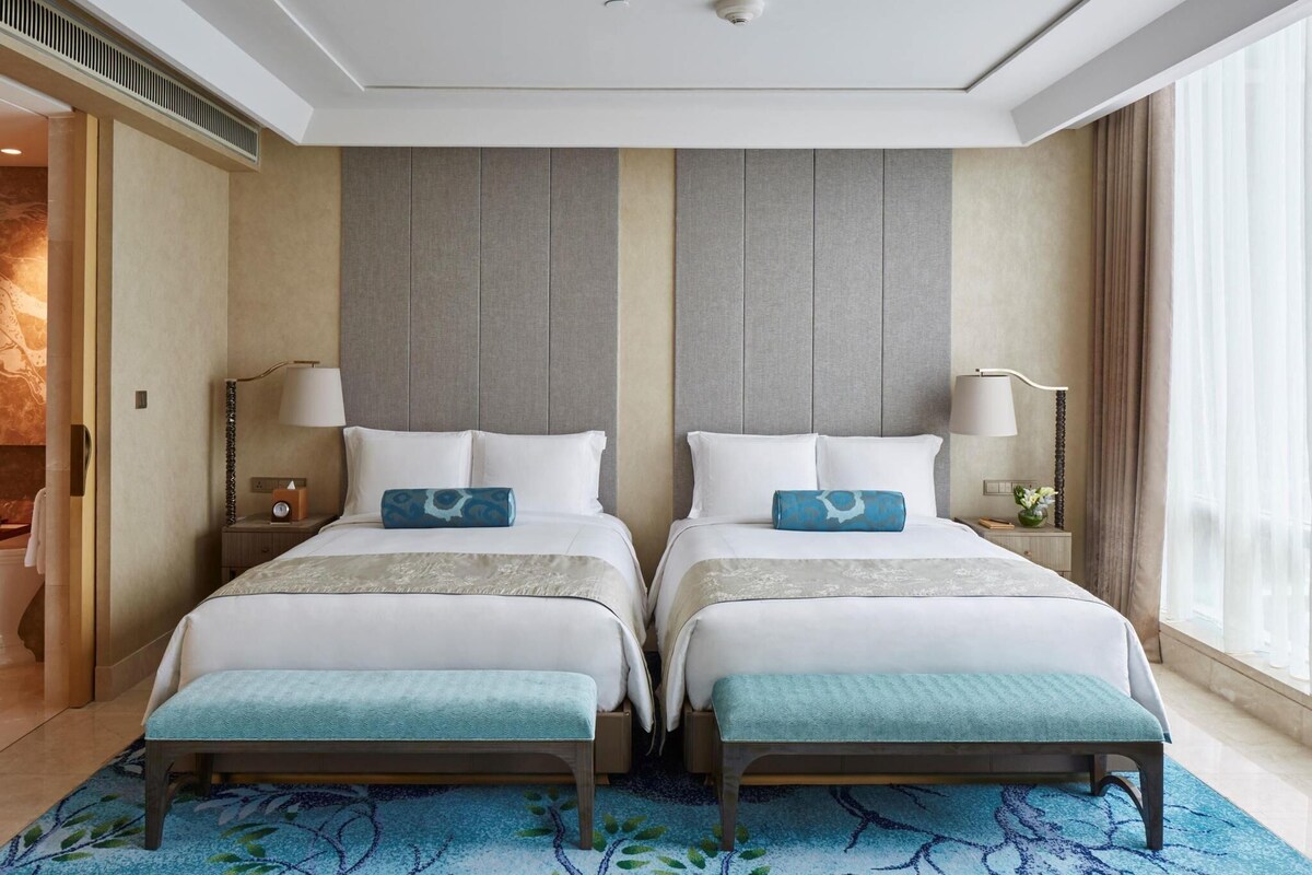 Habitación de hotel con dos camas, un tapete azul estampado y un ventanal con cortinas.