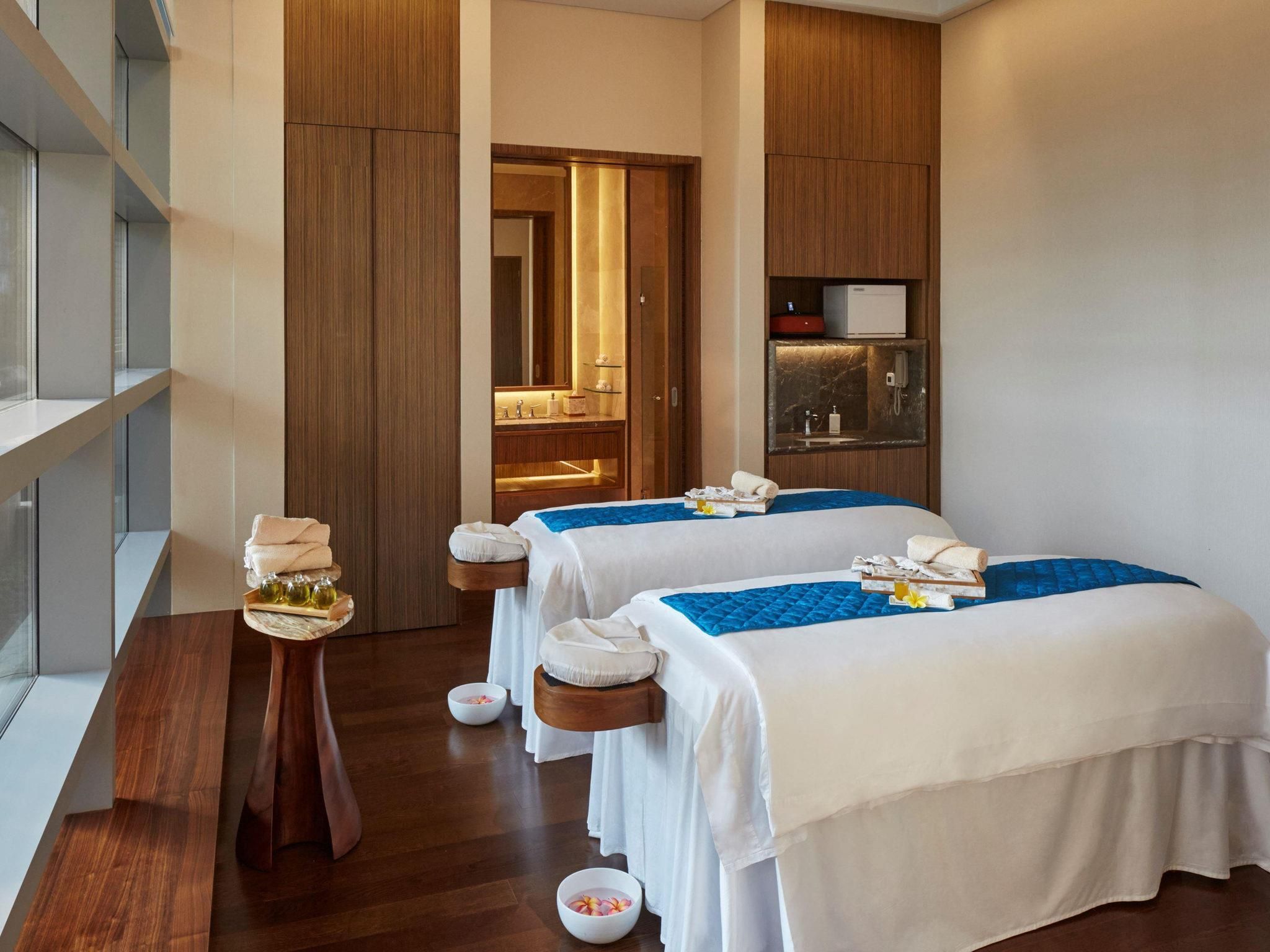 A hotel room with two beds, a wooden floor, a small table with toiletries, and a mirror.