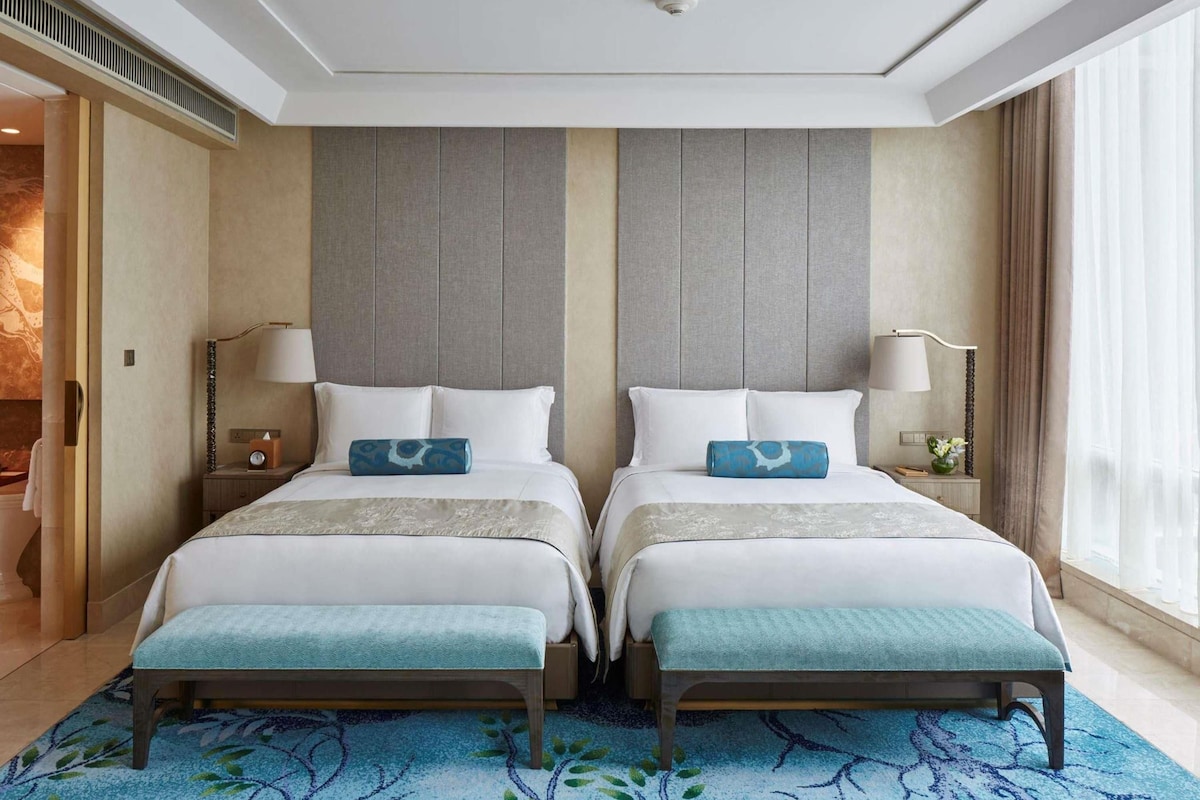 Una habitación de hotel con dos camas, un ventanal grande y una alfombra azul estampada.
