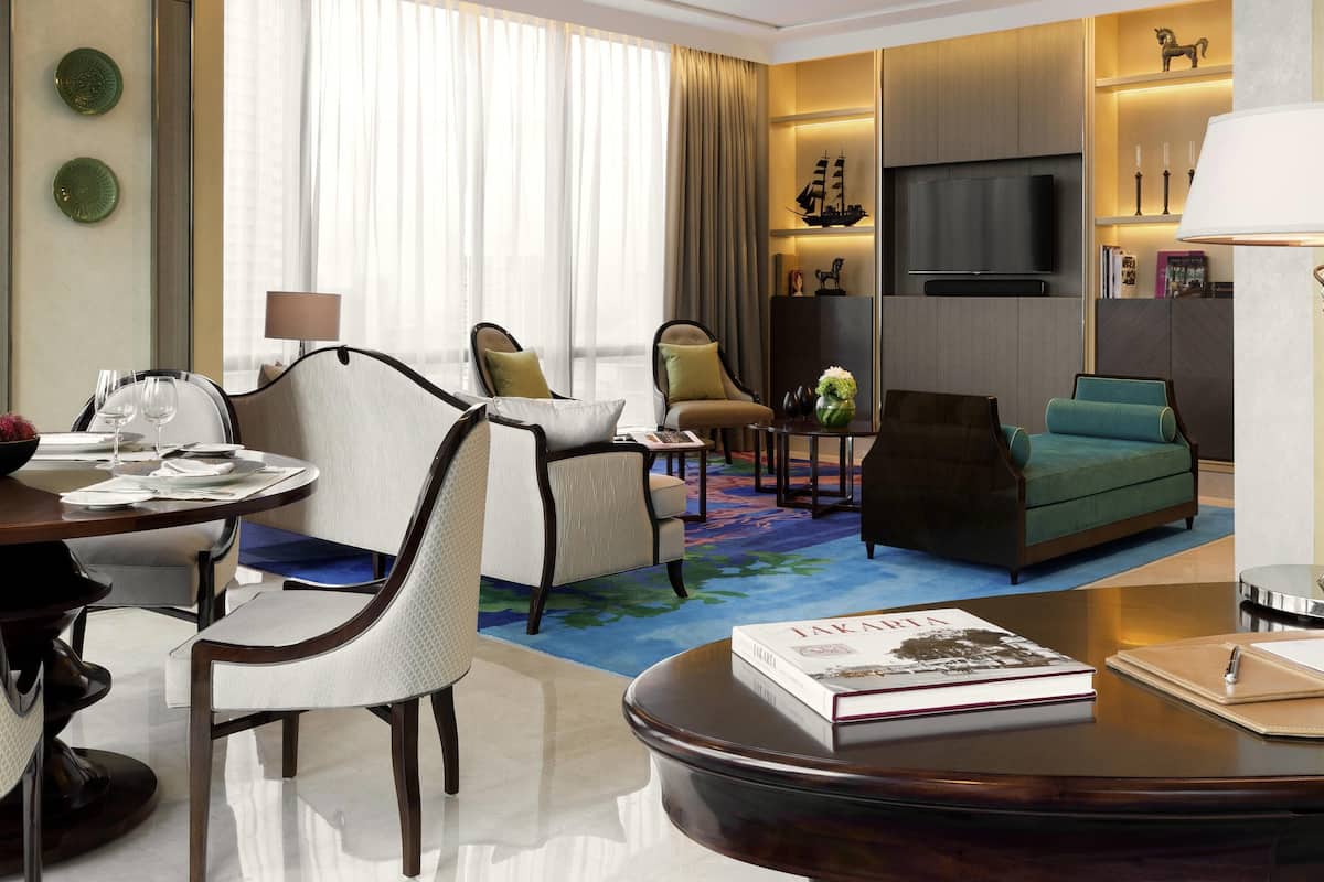 A hotel room with a dining area, a sofa, a TV, and a bookshelf.