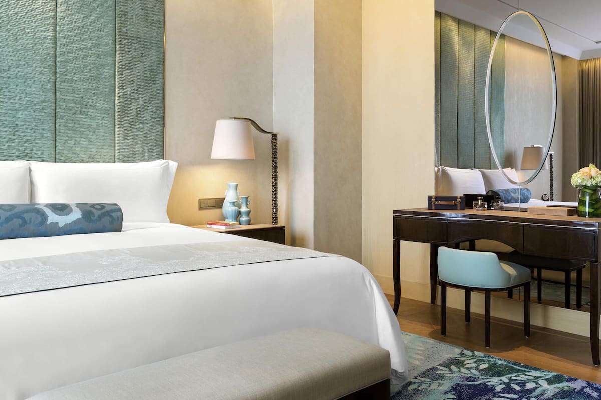 A hotel room with a bed, a desk, a chair, a lamp, and a mirror.